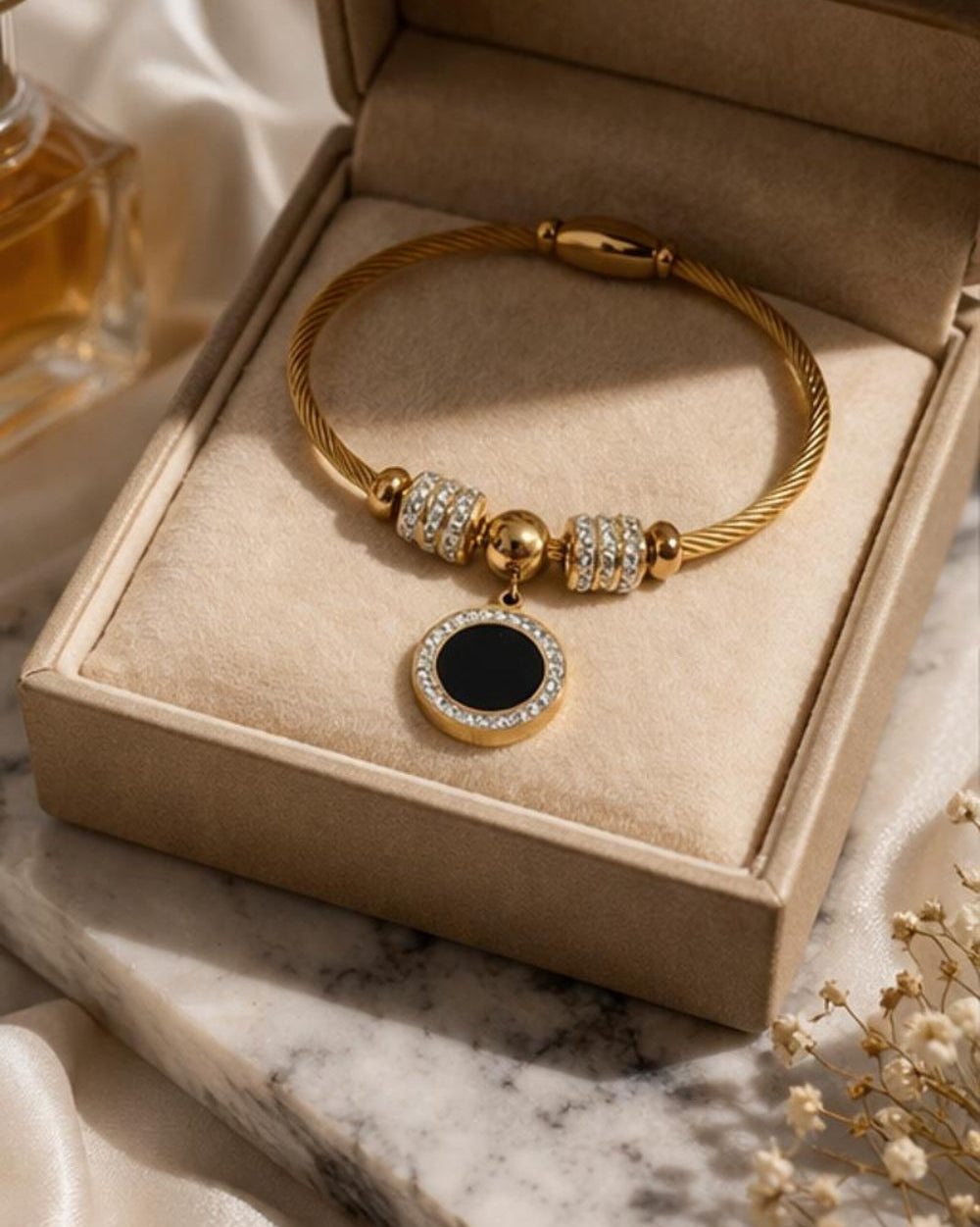 Gold plated stainless steel bangle bracelet with black enamel charm displayed in jewelry box elegant presentation