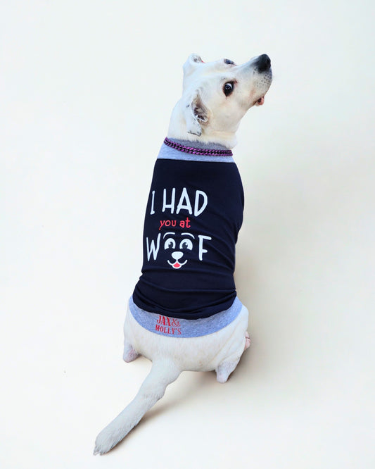 Back view of an adorable white dog modeling a navy Blue muscle tank with grey trim, featuring a graphic reading I Had You at Woof.