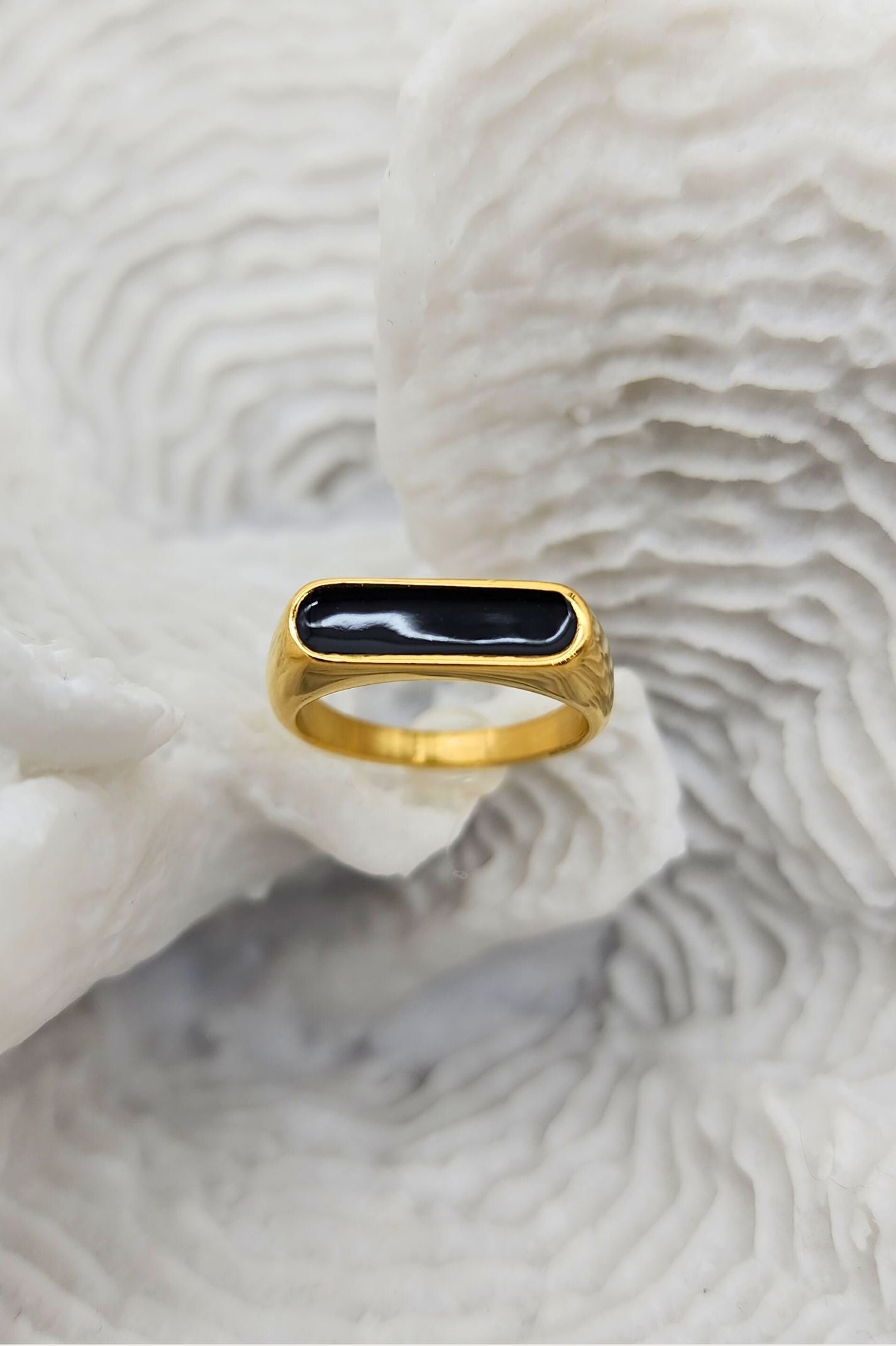 Stunning gold ring featuring a raised oblong black enamel setting that serves as its centerpiece on a white coral display.