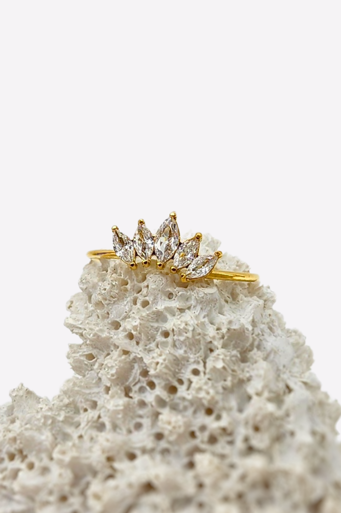 Stunning Regal Radiance ring with 5 sparkling gemstones resembling a crown, set on a delicate 18k gold plated band, artistically displayed on white coral for a striking effect.