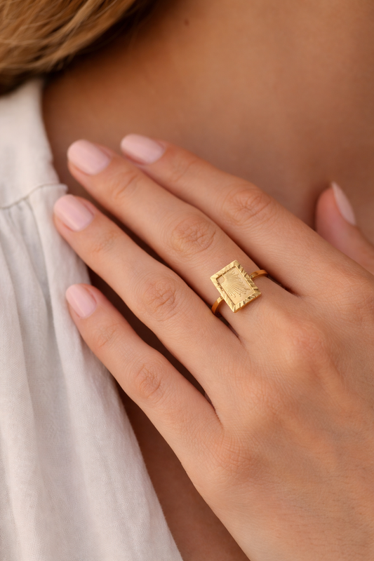 Gold PVD stainless steel sunburst signet ring on woman's finger close-up lifestyle view soft neutral background