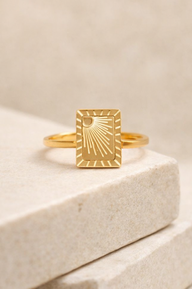 Gold PVD stainless steel sunburst signet ring on stone block studio product photo neutral background