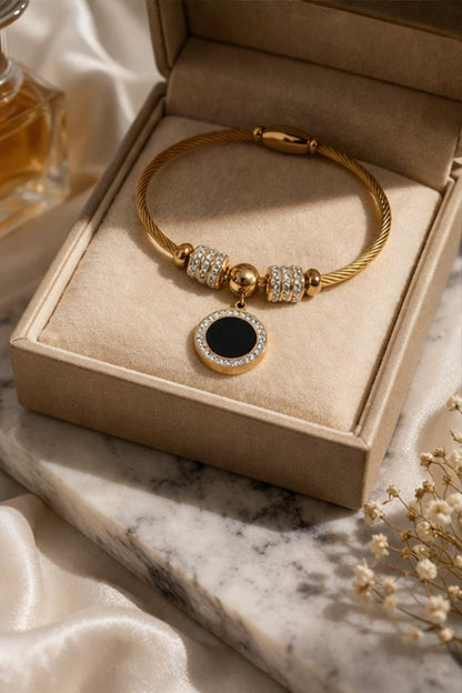 Gold plated stainless steel bangle bracelet with black enamel charm displayed in jewelry box elegant presentation