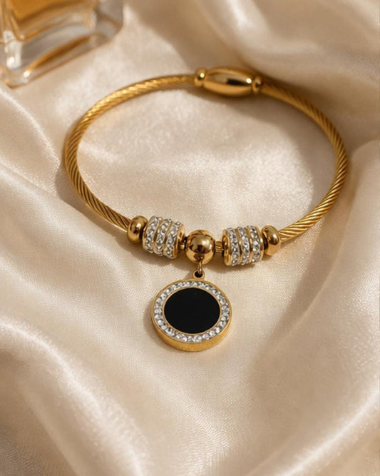 Gold plated stainless steel bangle bracelet with black enamel charm on soft silk fabric close up product view