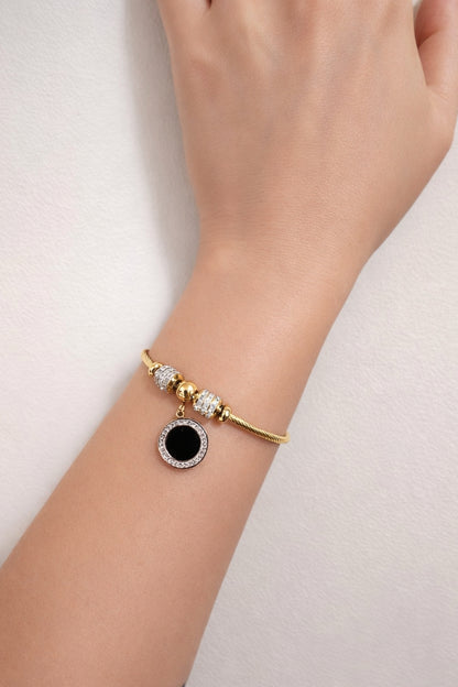 Gold plated stainless steel bangle bracelet with black enamel charm worn on wrist close up lifestyle view