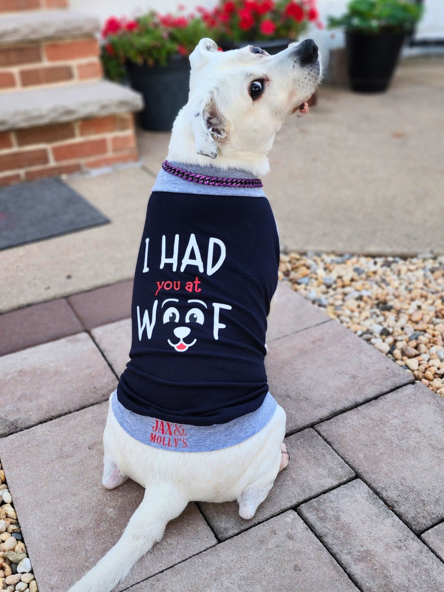 Back view of an adorable white dog modeling a navy Blue muscle tank with grey trim, featuring a graphic reading I Had You at Woof.
