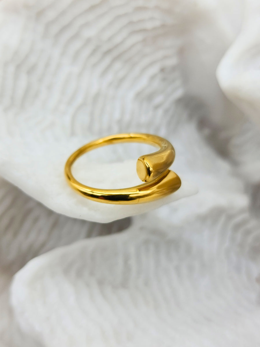 A exquisitely shiny, adjustable gold cuff ring displayed on white coral.