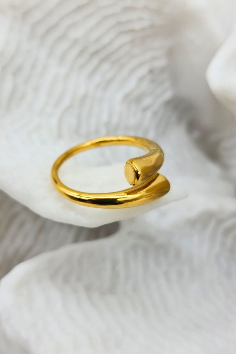 A exquisitely shiny, adjustable gold cuff ring displayed on white coral.