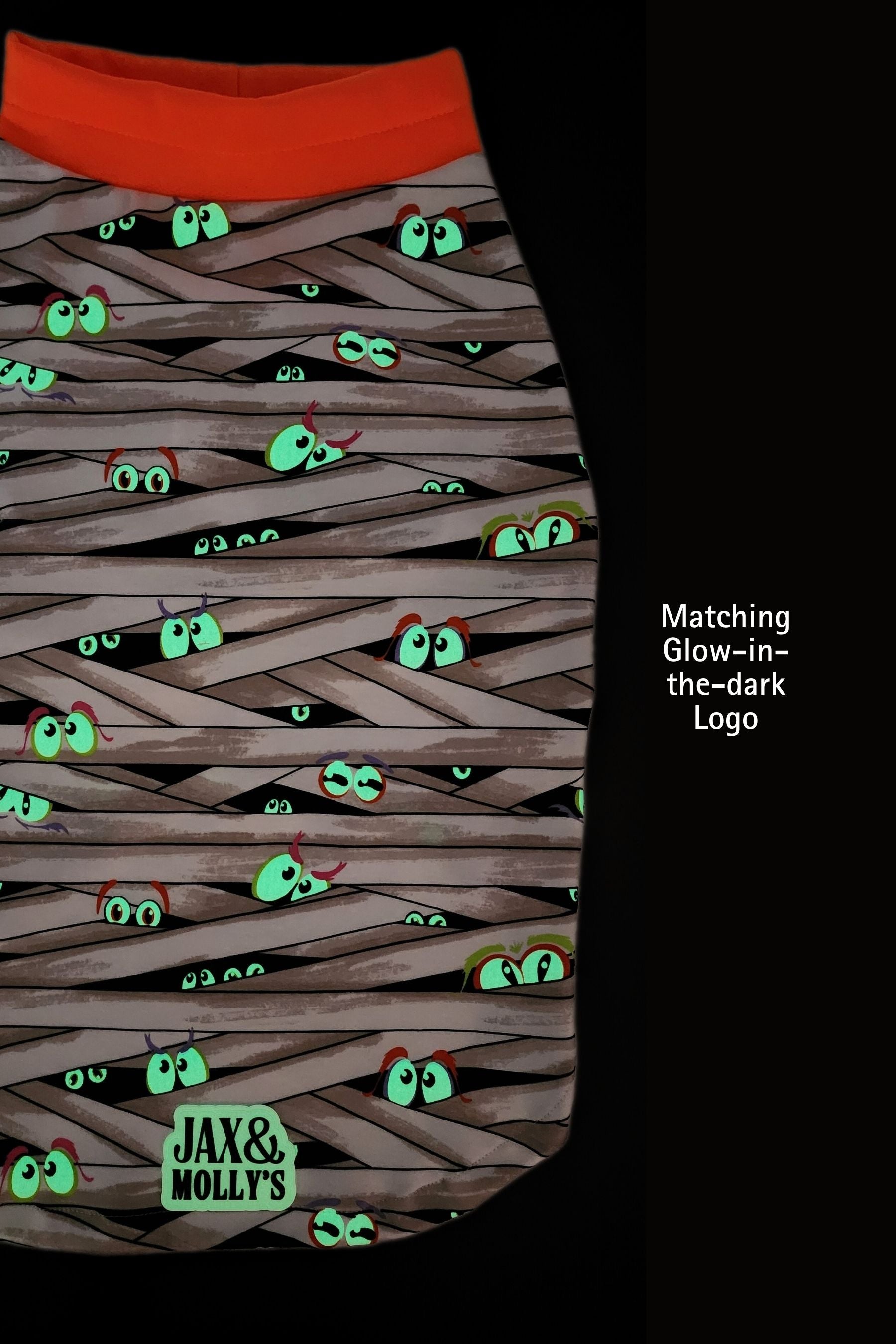 Glow-in-the-dark dog pajama with eyes peeking out from behind woven strands and 'Jax & Molly's' branding, set against a dark background.