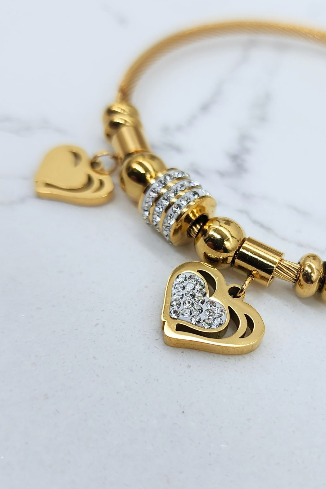 Close-up of Jax & Molly's 18k gold-plated Heart Duo Bracelet featuring a cable design with two exquisite heart pendants—one embellished with sparkling crystals and the other showcasing a brilliant gold shine.