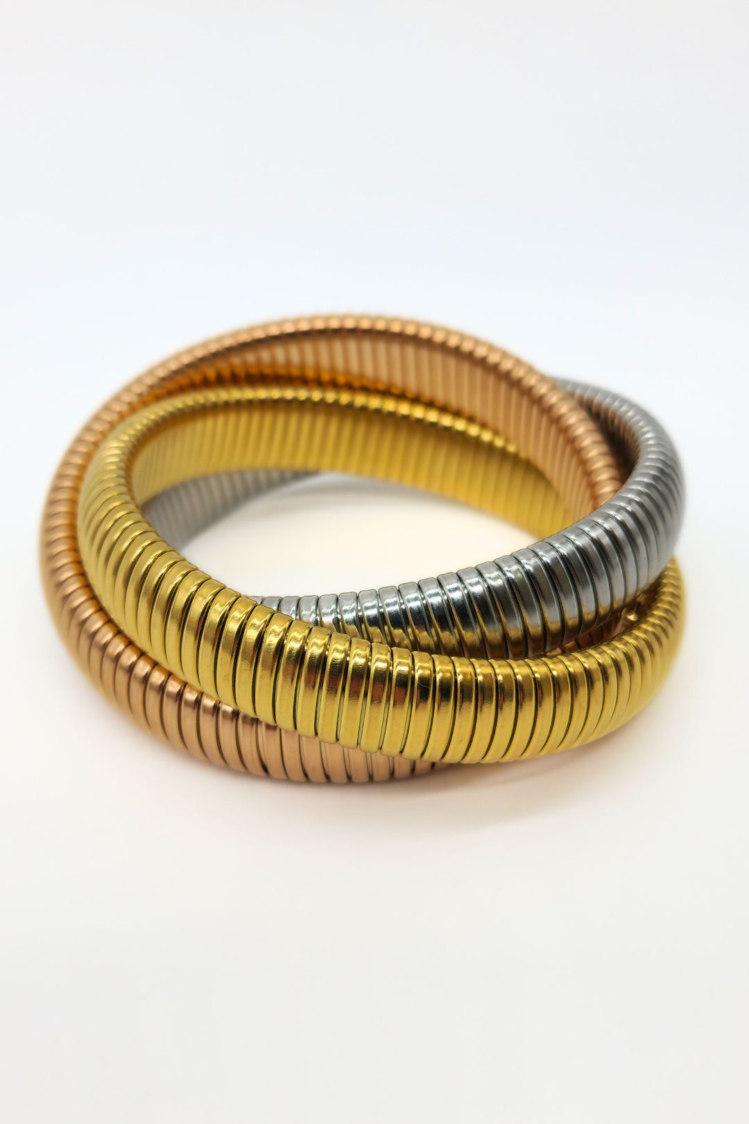 Close-up of three interlinked stretch snake bracelets in steel, rose gold, and gold.