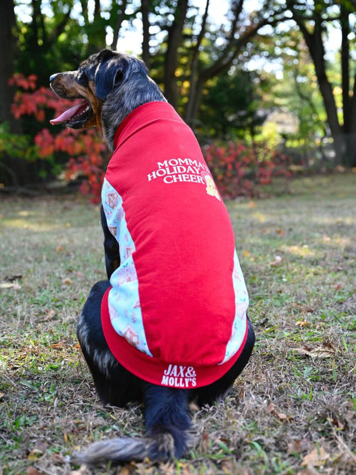 A rear view of dog wearing the Jax & Molly's 'Momma's Holiday Cheer' Dog Tank showcases a vibrant red fabric adorned with a white vinyl graphic that reads Momma's Holiday Cheer, accompanied by a gold gingerbread cookie design. The underbelly is a charming mint color, decorated with cute gingerbread houses.