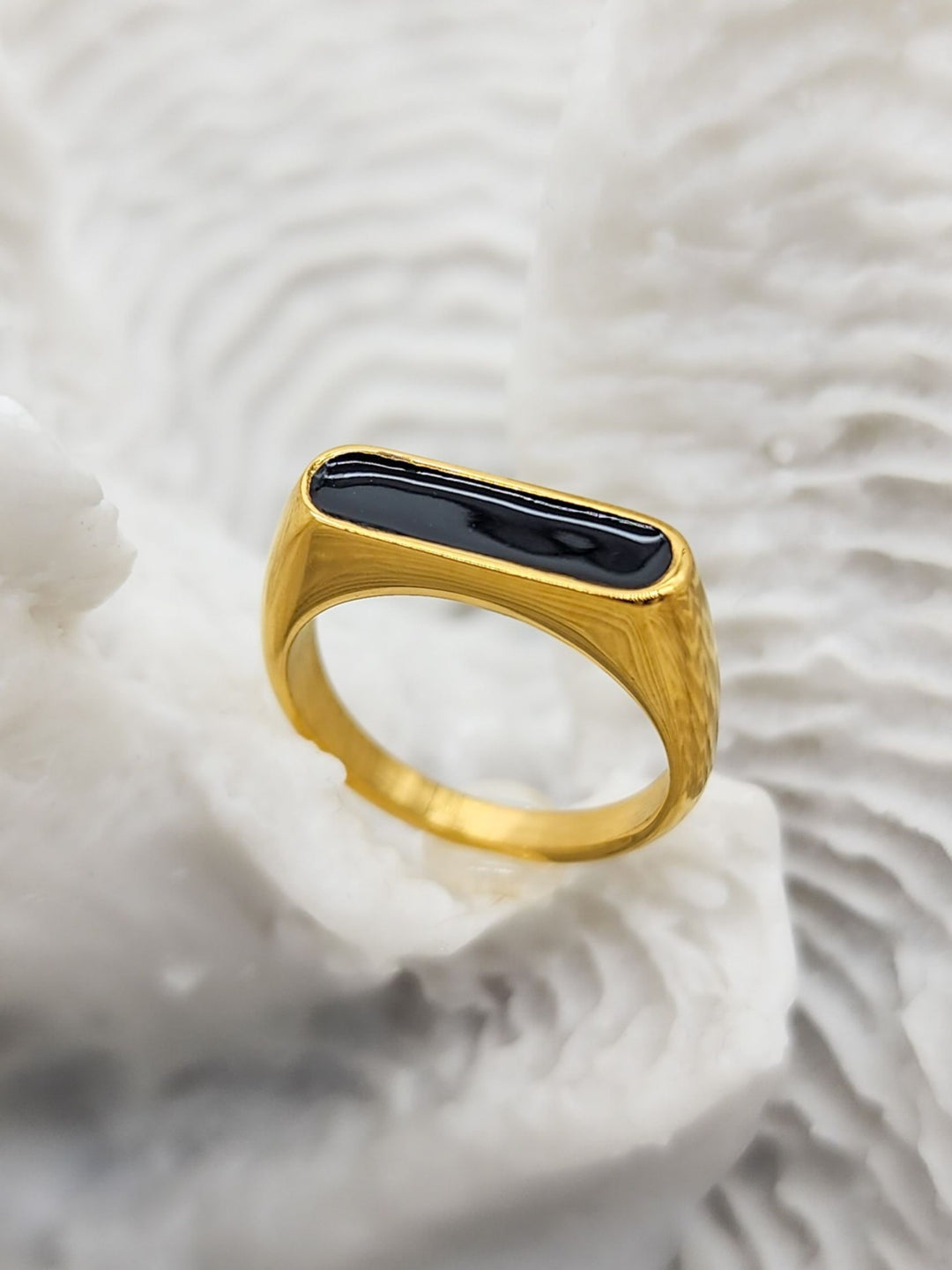 Stunning gold ring featuring a raised oblong black enamel setting that serves as its centerpiece on a white coral display.