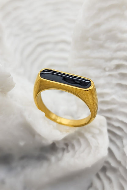 Stunning gold ring featuring a raised oblong black enamel setting that serves as its centerpiece on a white coral display.