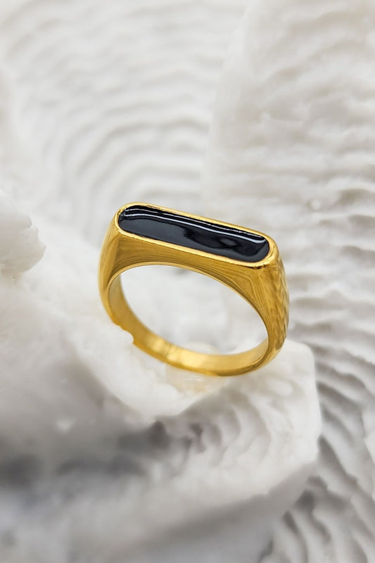Stunning gold ring featuring a raised oblong black enamel setting that serves as its centerpiece on a white coral display.