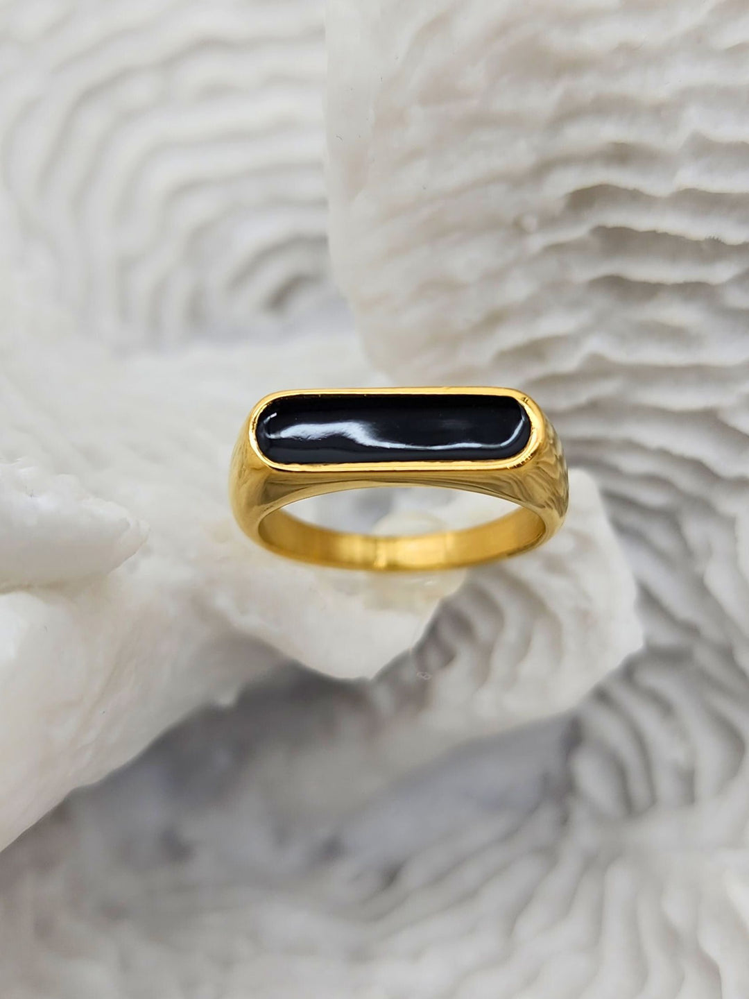 Stunning gold ring featuring a raised oblong black enamel setting that serves as its centerpiece on a white coral display.