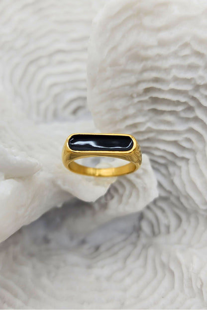Stunning gold ring featuring a raised oblong black enamel setting that serves as its centerpiece on a white coral display.