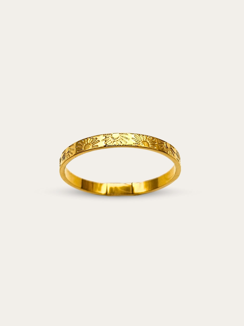 Front view of a gold band ring with intricate sun and ray engravings, showcased on a white backdrop.