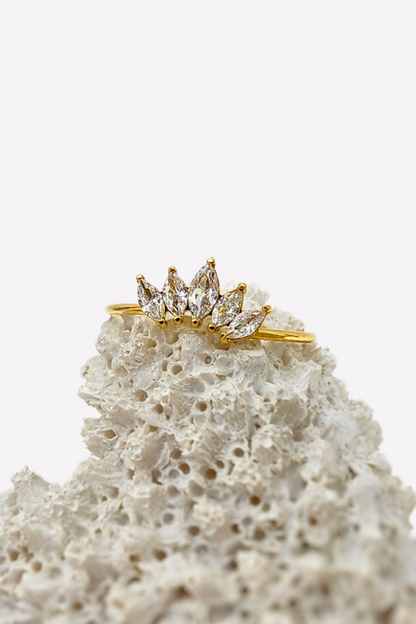 Stunning Regal Radiance ring with 5 sparkling gemstones resembling a crown, set on a delicate 18k gold plated band, artistically displayed on white coral for a striking effect.