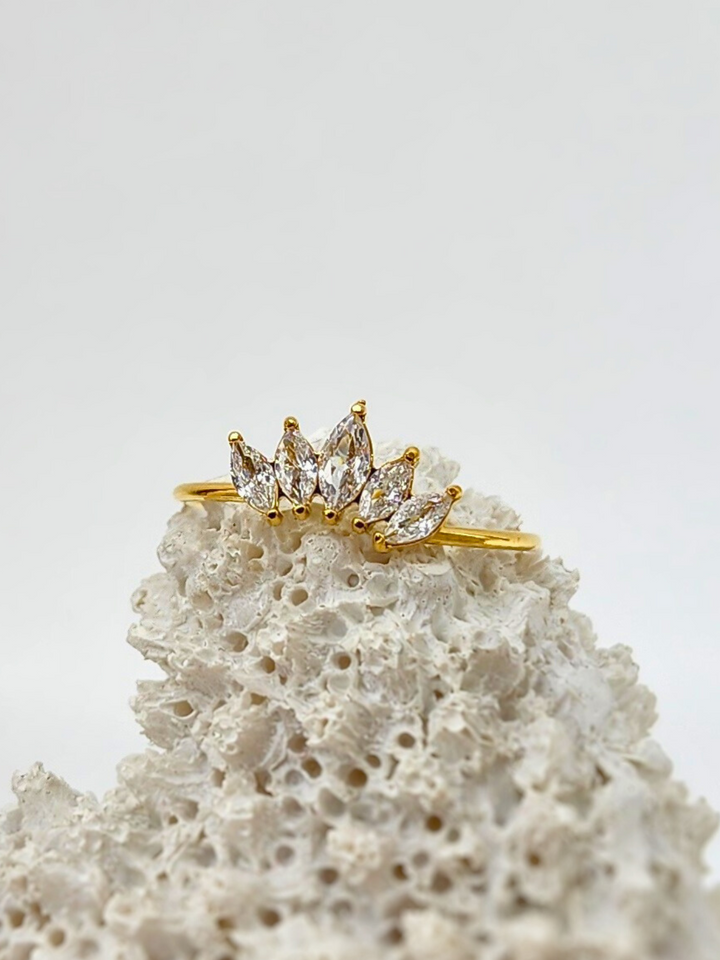 Stunning Regal Radiance ring with 5 sparkling gemstones resembling a crown, set on a delicate 18k gold plated band, artistically displayed on white coral for a striking effect.