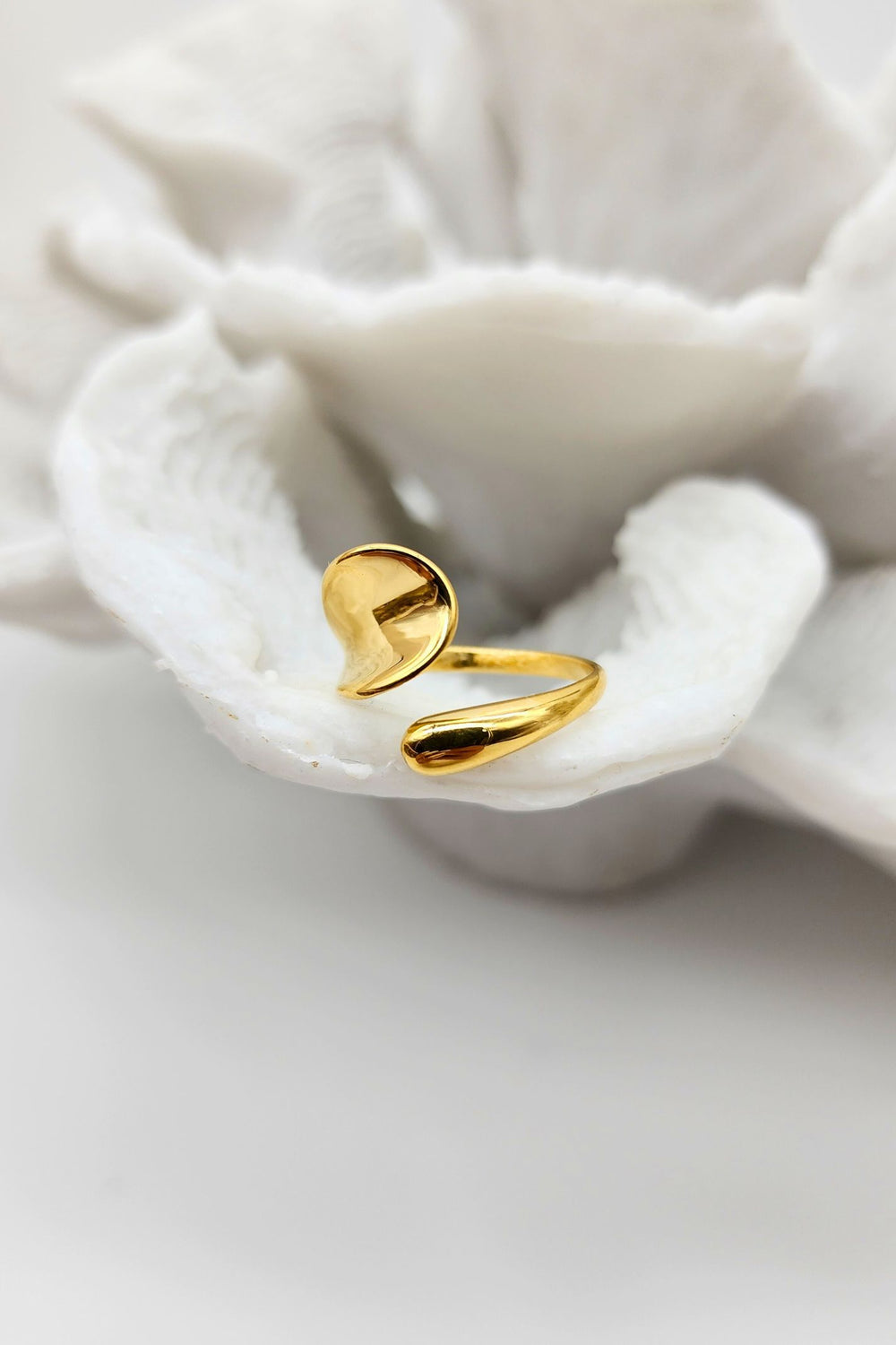 Gold ring with sleek adjustable design placed on white coral.