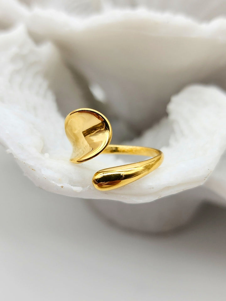 Gold ring with sleek adjustable design placed on white coral.