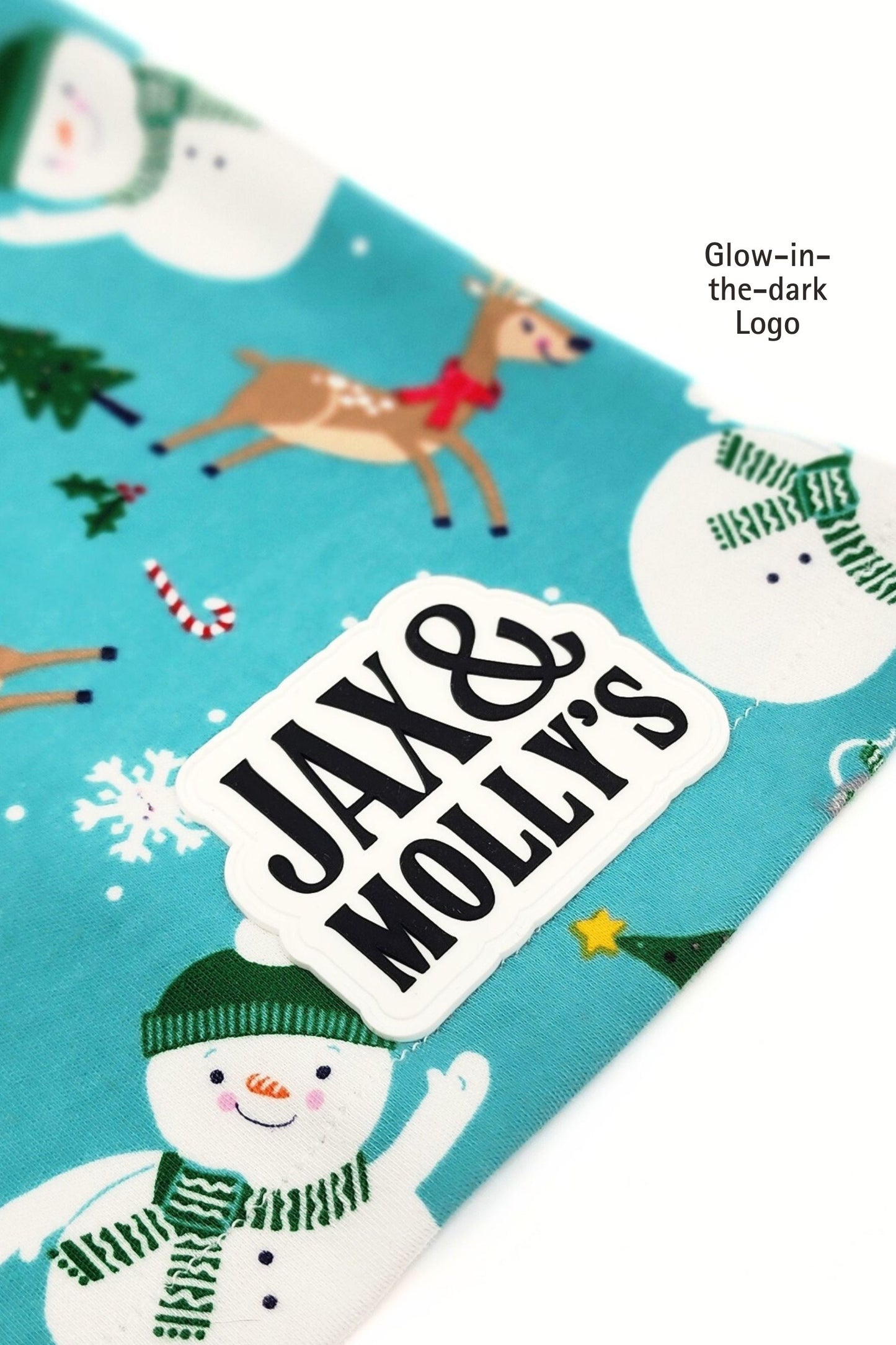 Close-up of a Glow-in-th-dark 'Jax & Molly's' label on a Snowman holiday-themed dog pajama shirt.