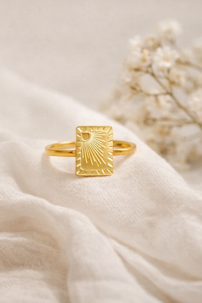 Gold PVD stainless steel sunburst signet ring on soft fabric with floral background studio product image