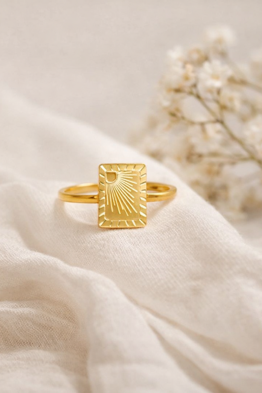 Gold PVD stainless steel sunburst signet ring on soft fabric with floral background studio product image
