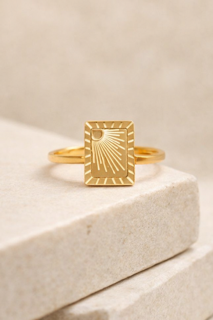 Gold PVD stainless steel sunburst signet ring on stone block studio product photo neutral background