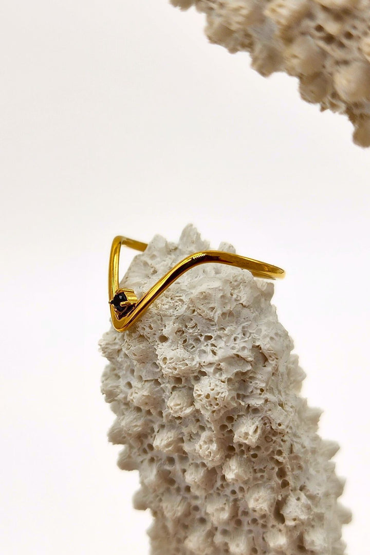 Thin v-shaped gold ring with black onyx stone at the tip on top of a white coral.