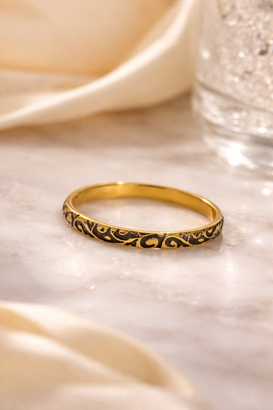 Black enamel filigree 18k PVD gold plated stainless steel band ring flat lay on marble surface soft luxury lighting