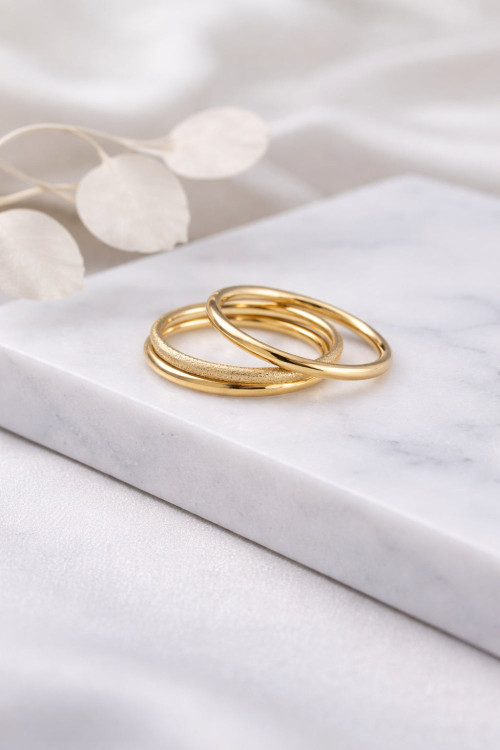gold stack ring set with three bands styled on marble surface showing polished and textured finishes