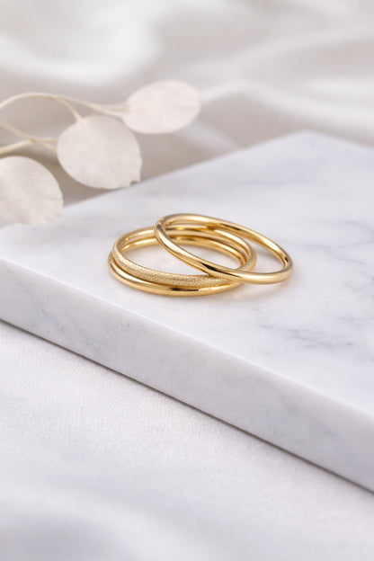 gold stack ring set with three bands styled on marble surface showing polished and textured finishes