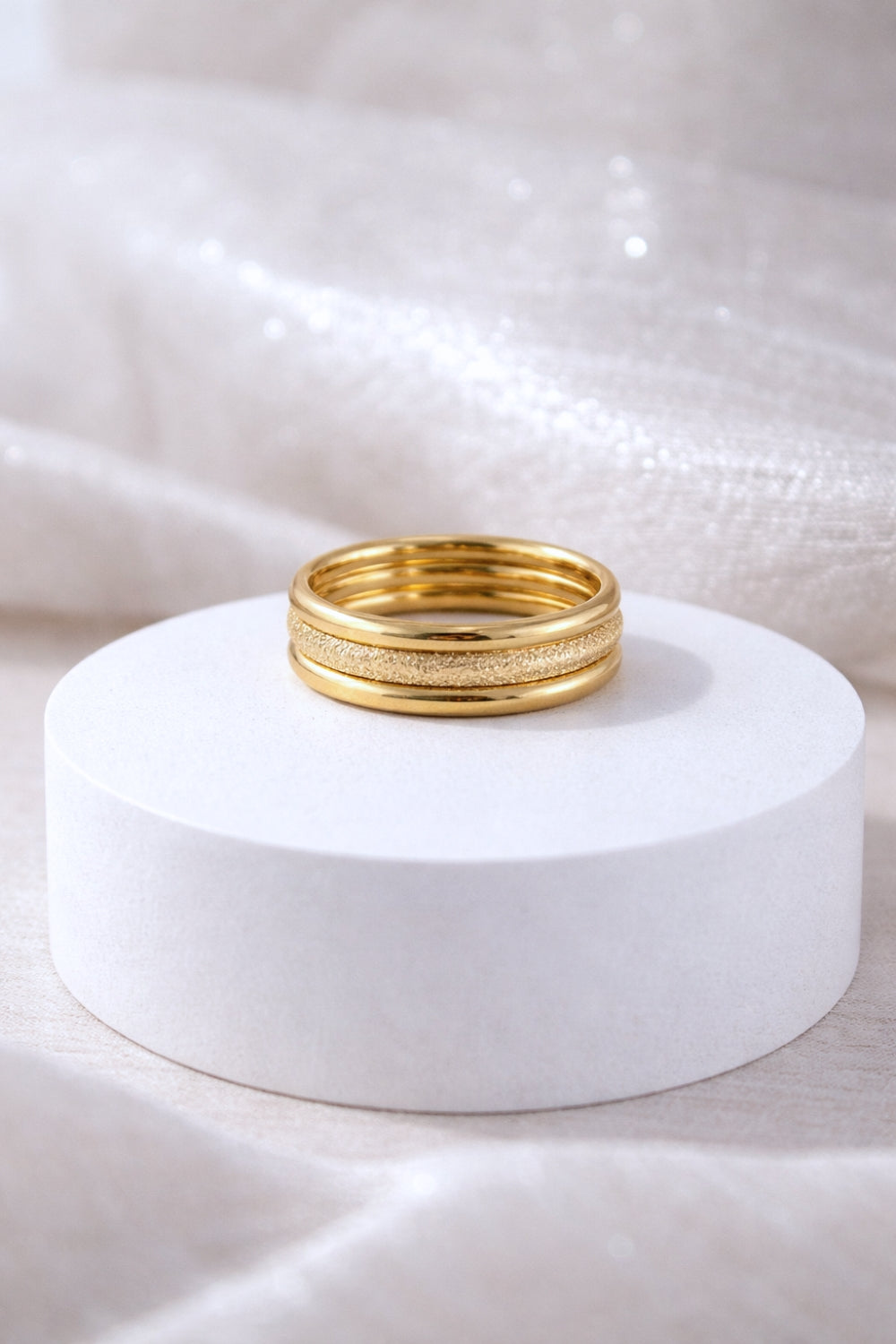 gold stack ring set with polished and textured bands displayed on white pedestal soft neutral background