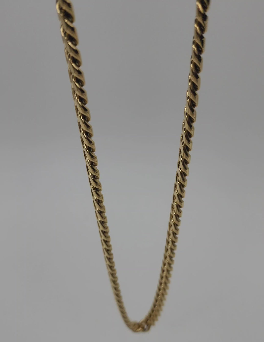 A close-up video of a 10mm gold color stainless steel Cuban link chain. The camera pans over the intricately designed links, showcasing their polished, reflective surface and smooth interlocking pattern. The gold color gleams under the light, highlighting the chain's luxurious and sturdy appearance. The video focuses on the clasp at the end, revealing its secure and robust design.