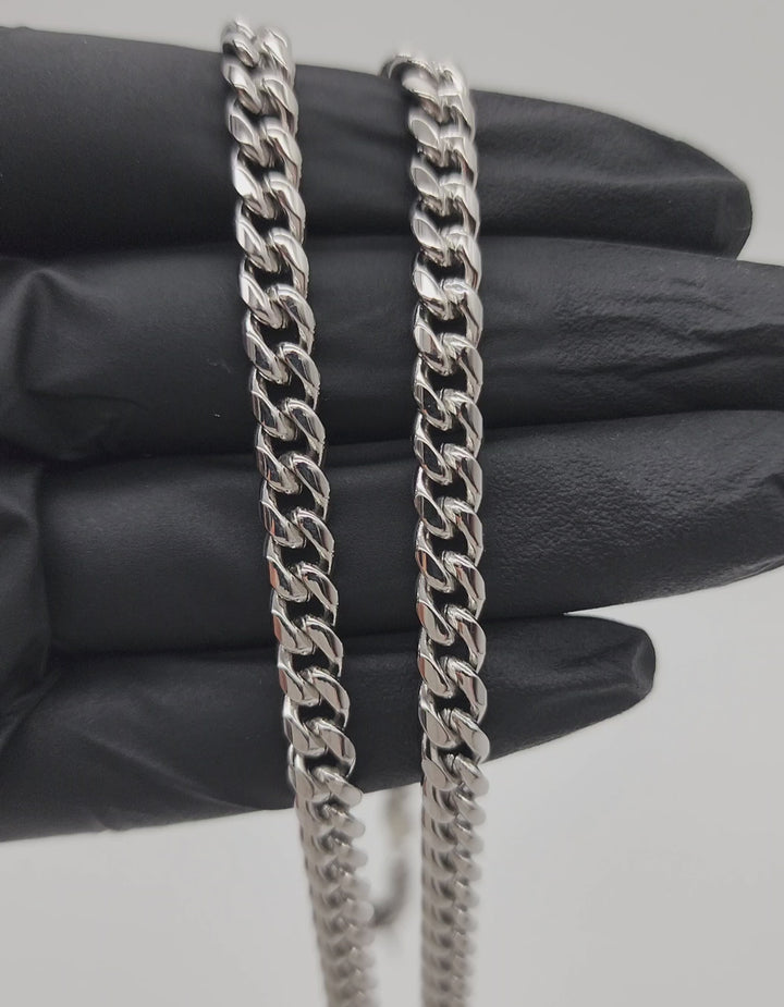 A close-up video of a 6mm silver-colored stainless steel Cuban link chain. The chain glistens under soft lighting, showcasing its interlocking links and smooth finish. The video pans slowly to highlight the chain's sleek design and durable craftsmanship.