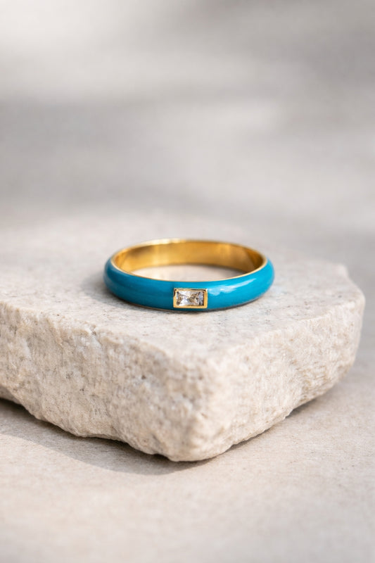teal enamel gold band ring with baguette stone flat lay on neutral stone surface